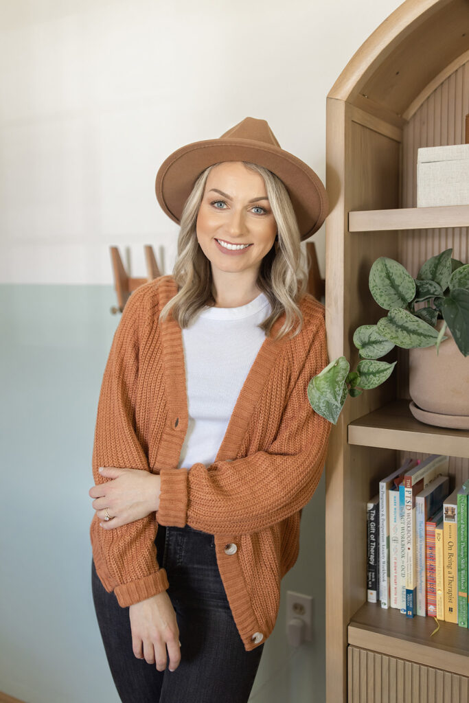 a woman wearing a hat and sweater leaning against a bookcase