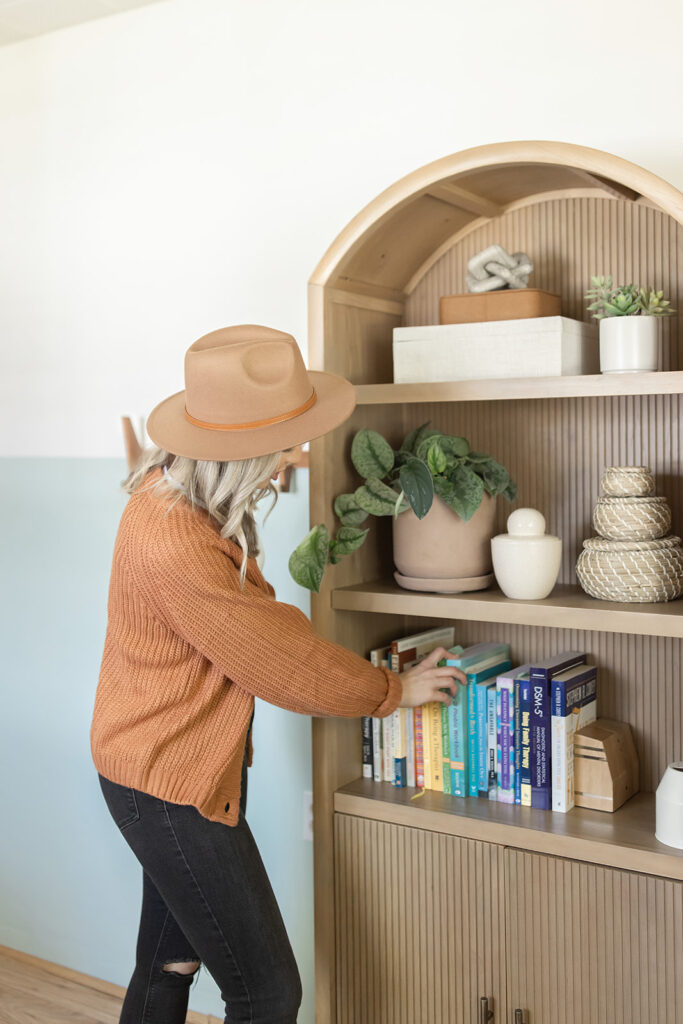 a woman in a hat picking a book from a shelf