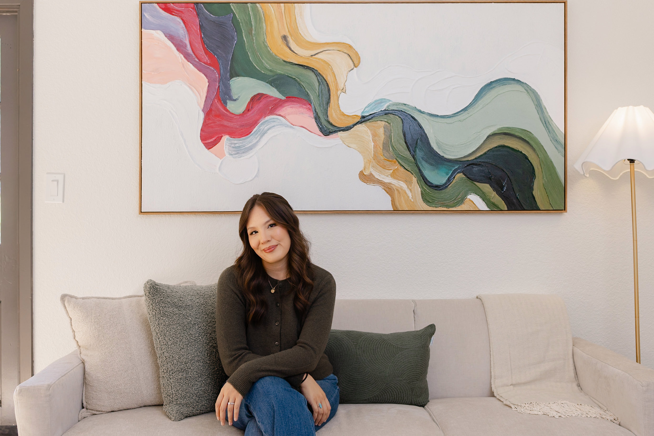 Woman sitting on a couch, artwork behind.